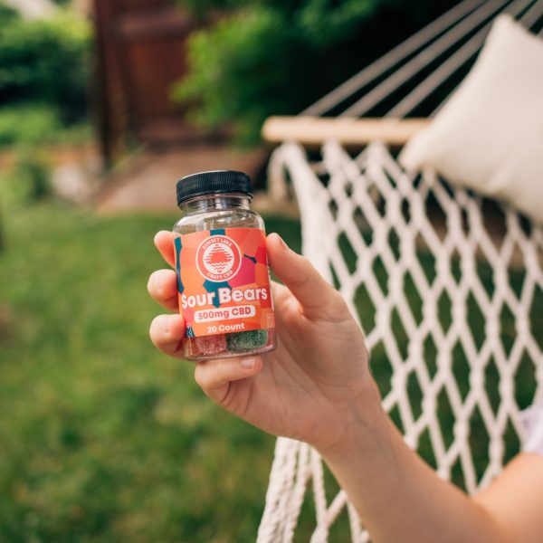 A hand holding up CBD Gummies while laying in a hammock