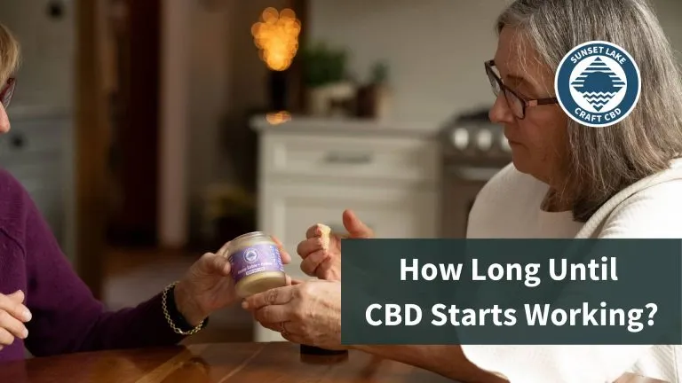 A woman, sitting at a table, rubs CBD Salve on her wrist. The text reads "How Long Until CBD Starts Working?"